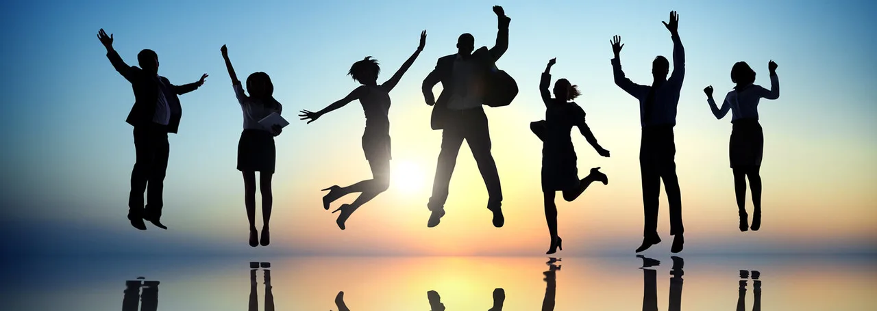 Silhouetten van een team dat juichend in de lucht springt bij zonsondergang